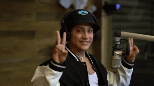 A Man Wearing Headphones And A Hat Giving The Peace Sign GIF