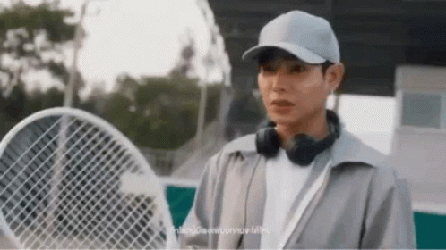 A Man Wearing Headphones And A Hat Is Holding A Tennis Racquet . GIF