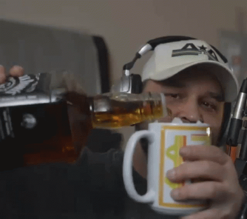 A Man Wearing Headphones And A Hat Is Pouring A Drink Into A Mug That Has The Letter A On It GIF