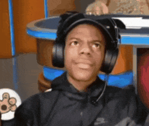 A Man Wearing Headphones And A Hat Is Sitting At A Table GIF