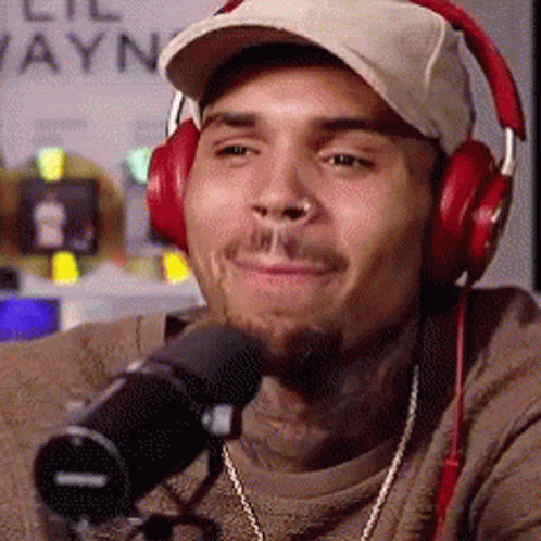 A Man Wearing Headphones And A Hat Is Sitting In Front Of A Microphone . GIF