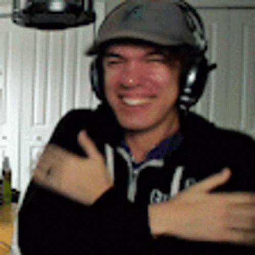 A Man Wearing Headphones And A Hat Is Smiling . GIF