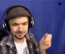 A Man Wearing Headphones And A Hat Is Standing In Front Of A Blue Wall . GIF