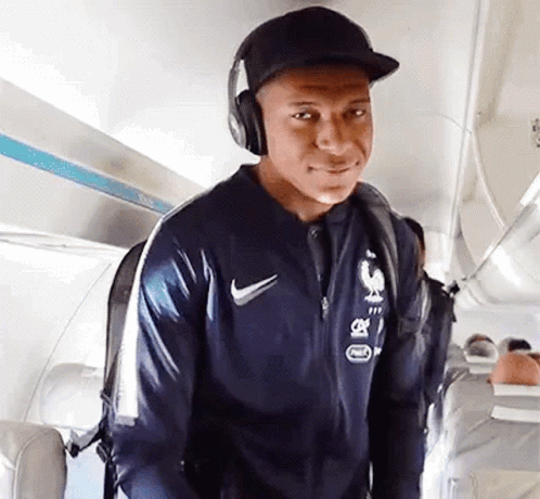 A Man Wearing Headphones And A Hat Is Walking On An Airplane . GIF