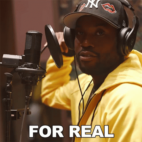 A Man Wearing Headphones And A Hat Stands In Front Of A Microphone With The Words " For Real " Written Below Him GIF