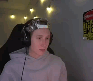 a man wearing headphones and a hat with tape on it is sitting in front of a sign that says danger .