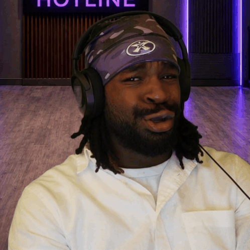 A Man Wearing Headphones And A Headband With The Word Hotline On The Wall Behind Him GIF