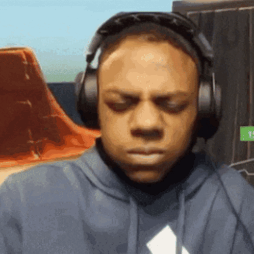 A Man Wearing Headphones And A Hoodie Is Making A Face . GIF