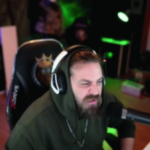 A Man Wearing Headphones And A Hoodie Is Sitting In Front Of A Microphone In A Gaming Chair GIF