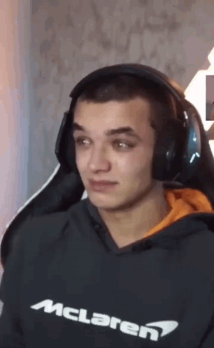 A Man Wearing Headphones And A Mclaren Sweatshirt Is Sitting In A Chair . GIF