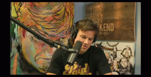 A Man Wearing Headphones And A Paid T-Shirt Is Sitting In Front Of A Microphone GIF