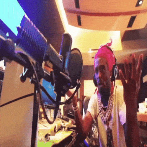 A Man Wearing Headphones And A Pink Headband Stands In Front Of A Microphone With His Hands In The Air GIF