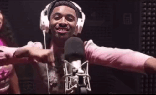 A Man Wearing Headphones And A Pink Shirt Is Standing In Front Of A Microphone GIF