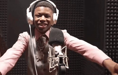 A Man Wearing Headphones And A Pink Shirt Is Standing In Front Of A Microphone GIF