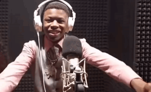 A Man Wearing Headphones And A Pink Shirt Is Standing In Front Of A Microphone GIF