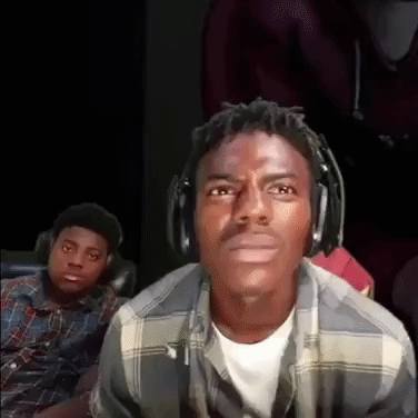 a man wearing headphones and a plaid shirt is looking at the camera while another man looks on .