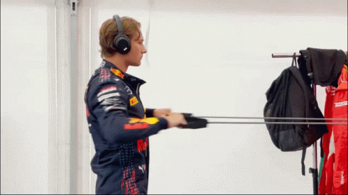 A Man Wearing Headphones And A Red Bull Jacket Reaches For A Backpack GIF