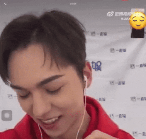 A Man Wearing Headphones And A Red Hoodie Is Smiling And Looking At The Camera . GIF