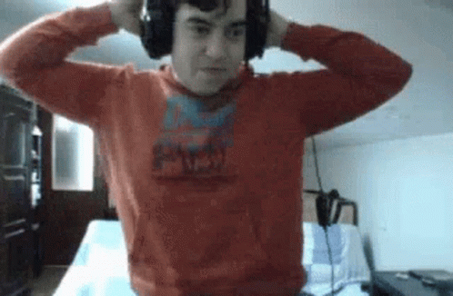A Man Wearing Headphones And A Red Sweater Is Standing In A Room . GIF
