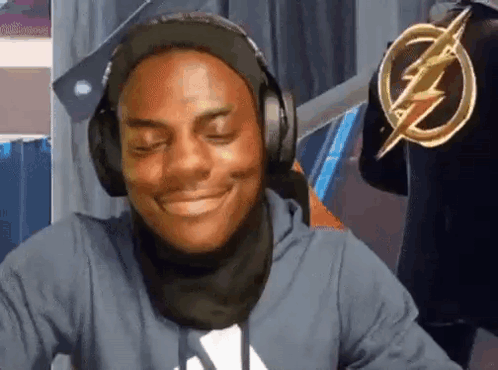 A Man Wearing Headphones And A Scarf Is Smiling And Looking At The Camera . GIF