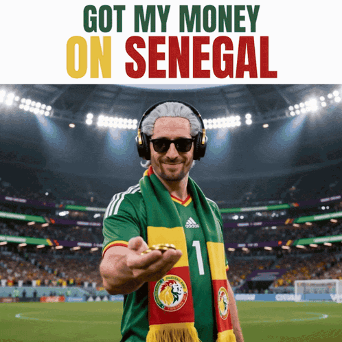 a man wearing headphones and a scarf with the number 1 on it holds a coin in front of a soccer field
