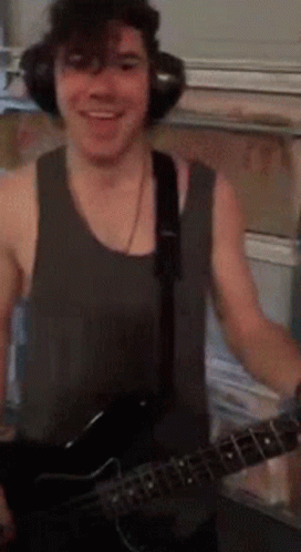 A Man Wearing Headphones And A Tank Top Is Holding A Guitar GIF