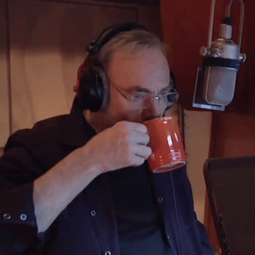 A Man Wearing Headphones And Glasses Is Drinking From An Orange Cup GIF