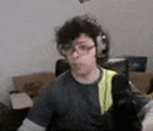 A Man Wearing Headphones And Glasses Is Sitting In A Living Room With A Cat . GIF