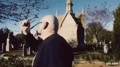 a man wearing headphones and glasses is standing in front of a church in a cemetery .