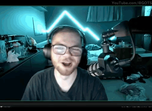 A Man Wearing Headphones And Glasses Stands In Front Of A Microphone With Youtube.com In The Corner GIF