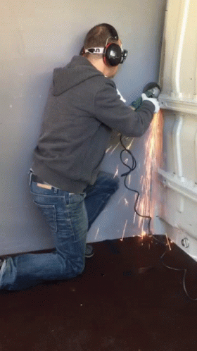 A Man Wearing Headphones And Goggles Is Using A Grinder To Cut A Piece Of Metal GIF