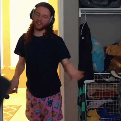 A Man Wearing Headphones And Pink Pajama Pants Is Standing In A Closet GIF