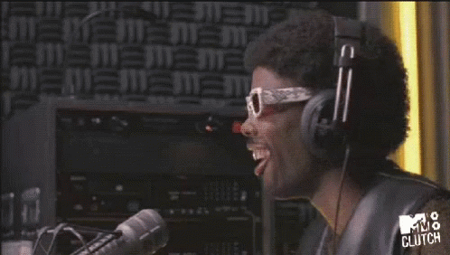 A Man Wearing Headphones And Sunglasses Is Laughing In Front Of A Mv8 Clutch Sign GIF