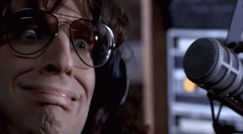A Man Wearing Headphones And Sunglasses Is Making A Funny Face In Front Of A Microphone . GIF