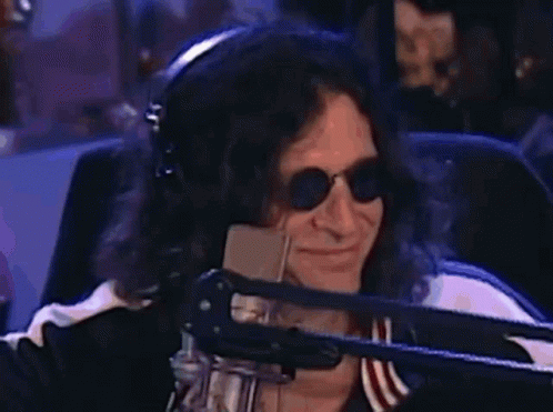 A Man Wearing Headphones And Sunglasses Is Smiling In Front Of A Microphone . GIF