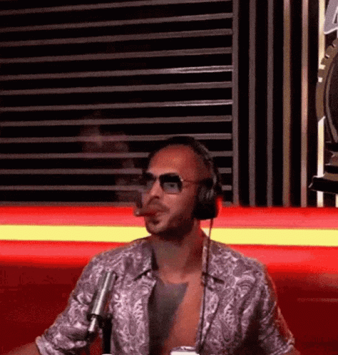 A Man Wearing Headphones And Sunglasses Is Smoking A Cigar While Sitting In Front Of A Microphone . GIF
