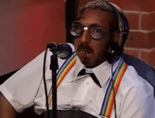 A Man Wearing Headphones And Suspenders Is Sitting In Front Of A Microphone . GIF