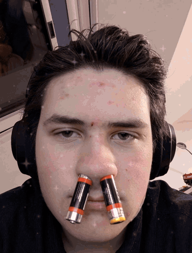 A Man Wearing Headphones Has Two Batteries On His Nose GIF