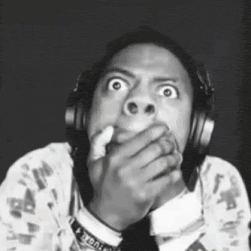 A Man Wearing Headphones Is Covering His Mouth With His Hand And Making A Funny Face . GIF