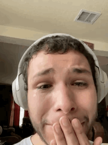 A Man Wearing Headphones Is Covering His Mouth With His Hand While Crying . GIF