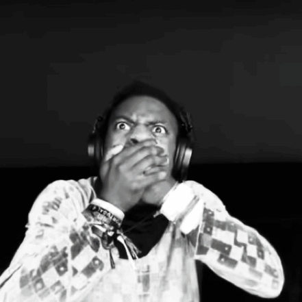 A Man Wearing Headphones Is Covering His Mouth With His Hands . GIF