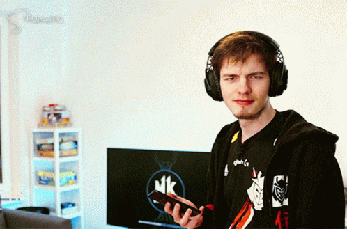 A Man Wearing Headphones Is Holding A Cell Phone In Front Of A Monitor That Says Mk On It GIF