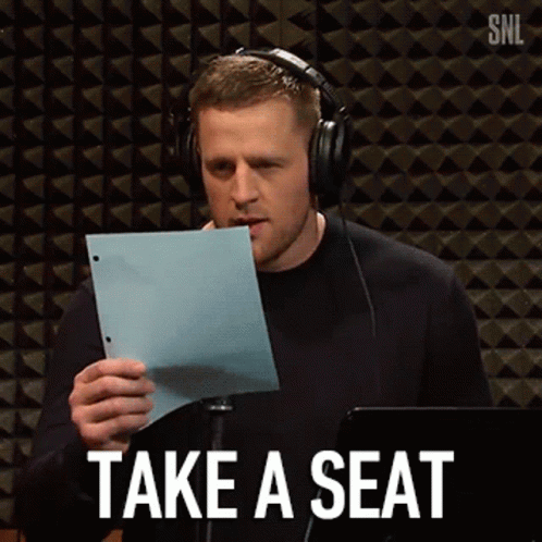 A Man Wearing Headphones Is Holding A Piece Of Paper With The Words Take A Seat Written On It . GIF