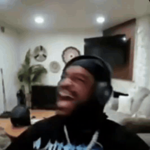 A Man Wearing Headphones Is Laughing In A Living Room While Sitting On A Couch . GIF