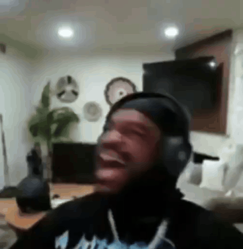 A Man Wearing Headphones Is Laughing In A Living Room While Sitting On A Couch . GIF