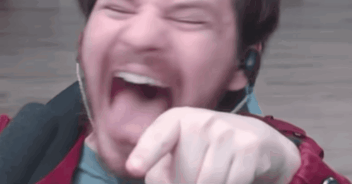A Man Wearing Headphones Is Laughing With His Mouth Open And Pointing At The Camera . GIF