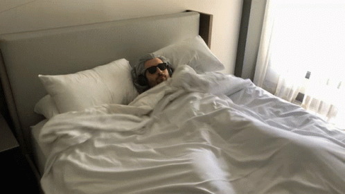 A Man Wearing Headphones Is Laying On A Bed GIF