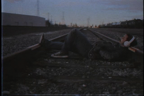 a man wearing headphones is laying on the train tracks