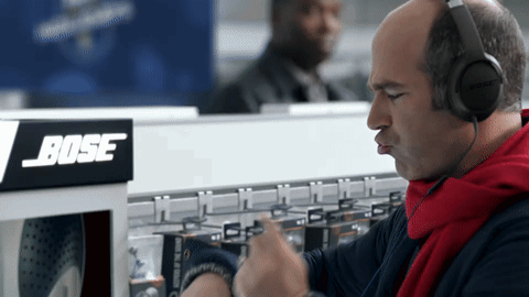 A Man Wearing Headphones Is Looking At His Watch In Front Of A Bose Sign GIF