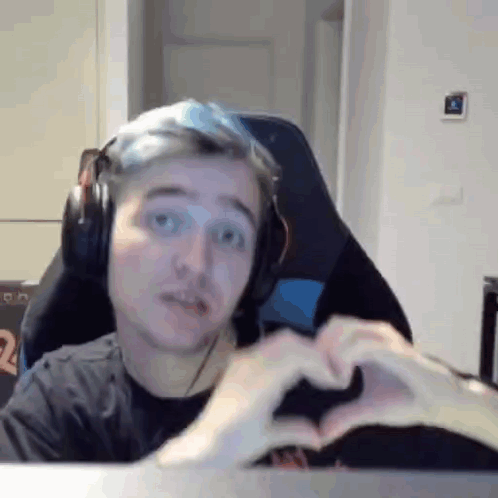 A Man Wearing Headphones Is Making A Heart With His Hands While Sitting In A Chair . GIF